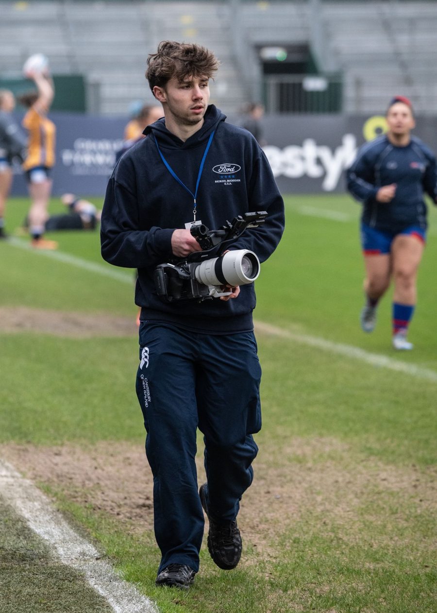 Ruaraidh walking the touchline at a stadium with his camera